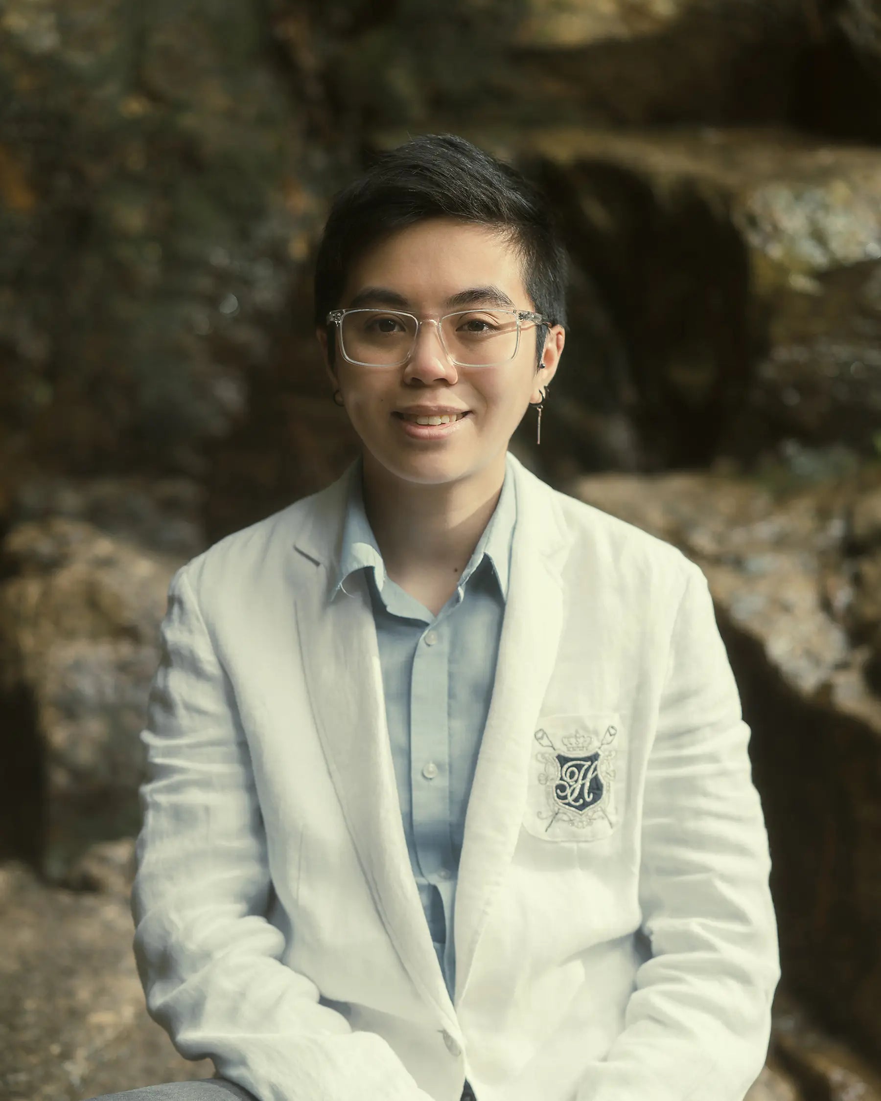 Den's cofounder, Shay, wearing glasses and a light-colored blazer, sitting outdoors.