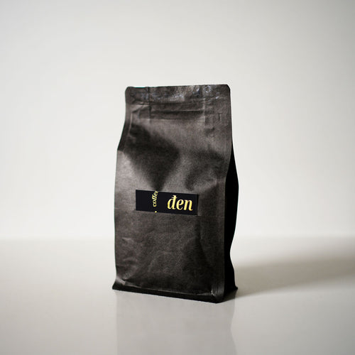 A sealed, black pouch of coffee beans labeled 'den' positioned against a white background.