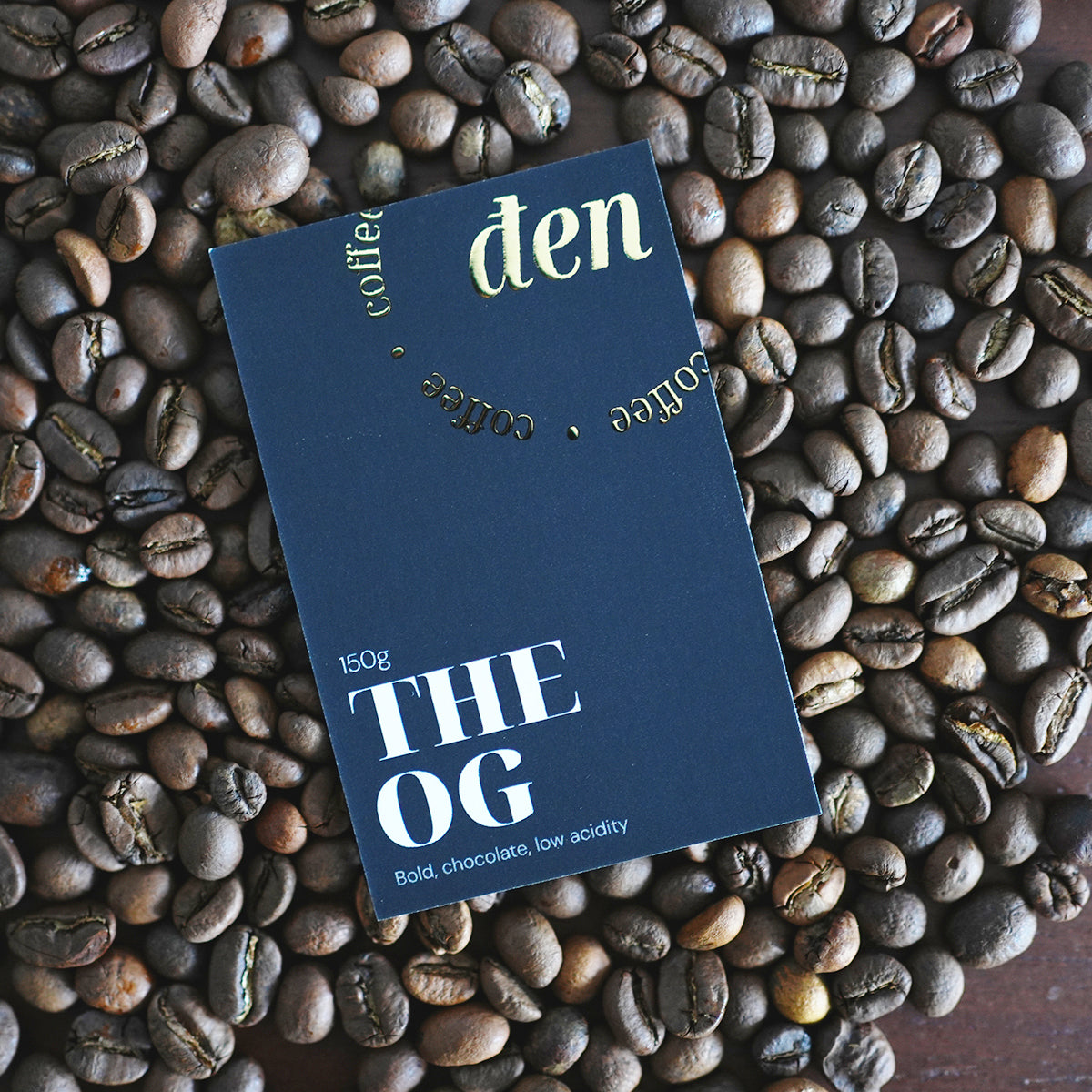 Coffee package labeled 'den Coffee' on a bed of coffee beans